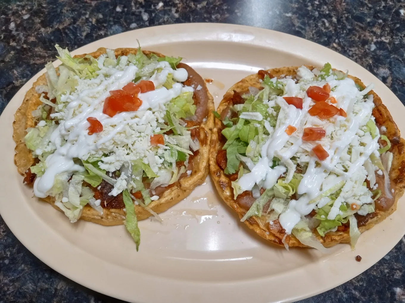 Two sopes topped with lettuce, cheese, crema and tomato
